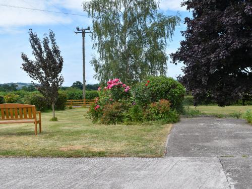 a park with a bench and a bush with pink flowers at Pheasant Pens 1 - Uk50187 in Llandenny