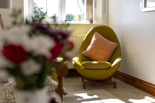 a yellow chair with a pillow in a living room at Drefach - Refurbished farmhouse in stunning surroundings with hot tub in Llanwinio