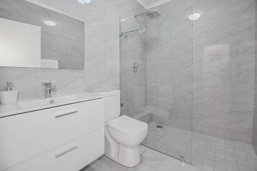 Un baño blanco con inodoro y ducha. en Modern Coastal Condo in Big Bay, en Cape Town