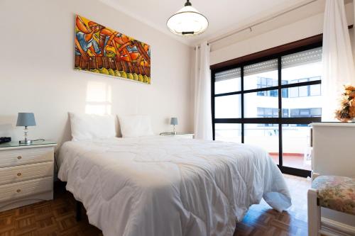 a bedroom with a white bed with a painting on the wall at Blue Bay Apt - São Martinho do Porto in São Martinho do Porto