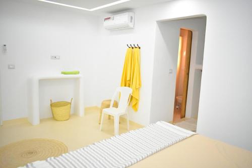 a white room with a white chair and a yellow curtain at VILLA SALAM, Maison D'hôte in Mezraya