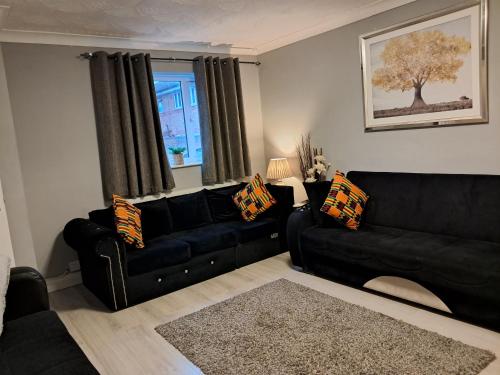 a living room with a black couch and a window at FANTASTIC COZY 3bed Hse London ExCEL Free Parking WIFI Sleeps 6 in London