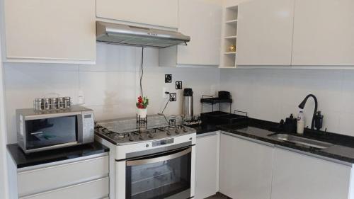 eine weiße Küche mit einem Herd und einer Mikrowelle in der Unterkunft Novíssima - Casa de Temporada a 09min do Thermas in Olímpia