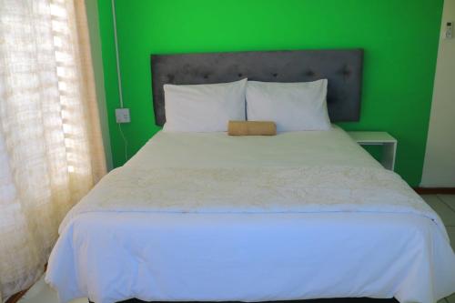 a green bedroom with a white bed with a green wall at Elite Stay Guest House in Rustenburg