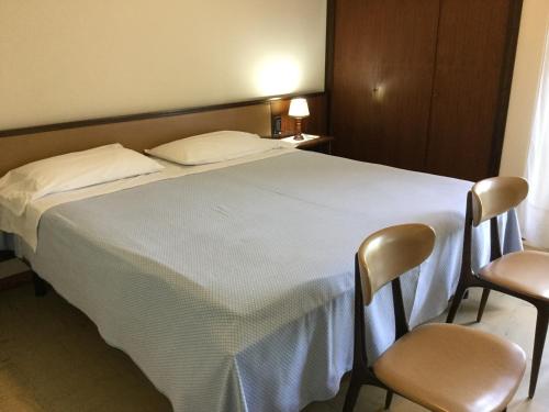 a bedroom with a white bed with two chairs at Hotel Terme Vulcania in Montegrotto Terme