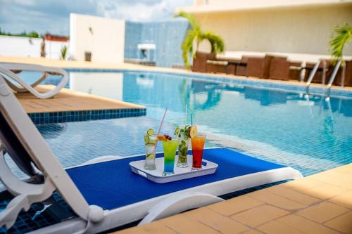 ヤムスクロにあるHotel Yatchenin Yamoussoukroのスイミングプールの横のテーブルにトレイ(ドリンク付)
