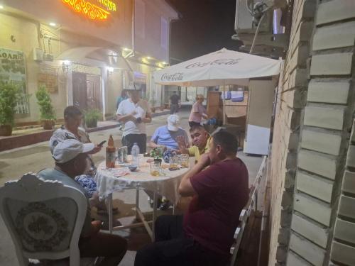 eine Gruppe von Menschen, die in einem Restaurant um einen Tisch herum sitzen in der Unterkunft Uncle Kolya Hotel str M Azam 39 in Buxoro
