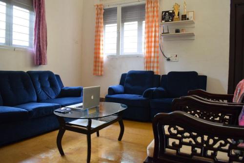 a living room with blue couches and a laptop on a table at Kamshet Lakeside Serene Artist Villa in Somavadi