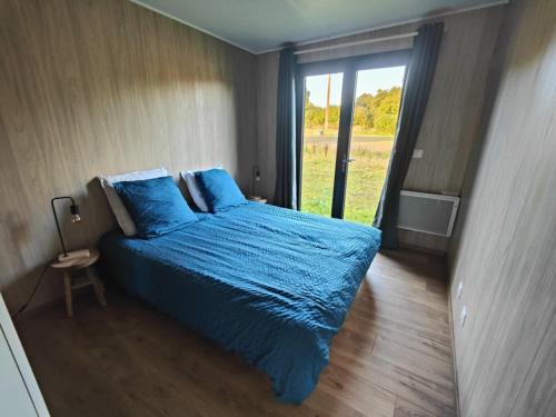 a bedroom with a bed with blue sheets and a window at La Cabane du Gouët in Saint-Julien