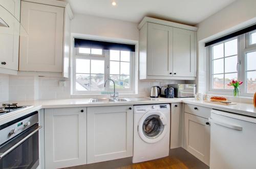 a kitchen with white cabinets and a washing machine at Sands in Swanage