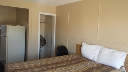 a bedroom with a bed with white pillows and a refrigerator at TC Motel in Medicine Hat