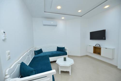 a living room with a blue couch and a tv at Dar Hella Apartments in El Maamoura