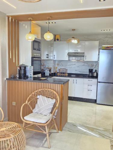 a kitchen with a counter and a chair and a refrigerator at Blue Bay Village Appartement Cocooning en Rez-de-Jardin avec Vue Mer dans une Résidence Sécurisée à Moulay Abdallah près El Jadida in Moulay Abdallah