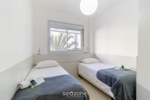 two beds in a room with a window at Apto c/ Churrasqueira em Cond. c/ Piscina BRI0102 in Florianópolis