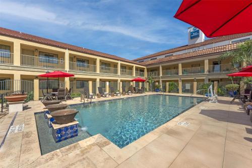 a pool in front of a hotel with red umbrellas at Best Western San Isidro Inn in Laredo