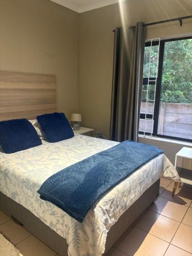 a bedroom with a bed with blue pillows and a window at Su Casa Port Alfred in Port Alfred