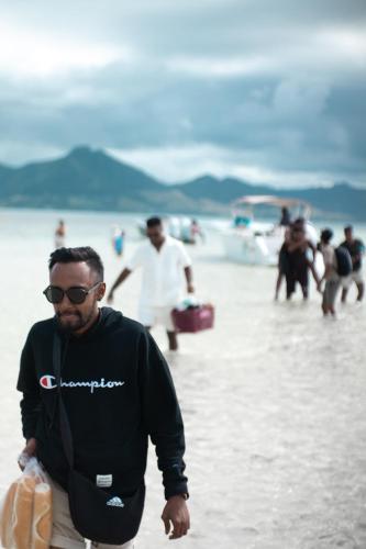 a man walking on the beach with people in the water at Pixel Cruise in Trou dʼ Eau Douce