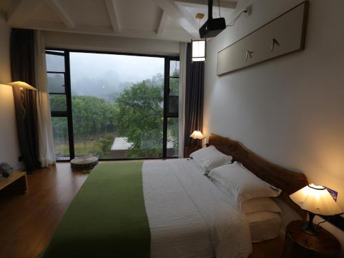 a bedroom with a bed with a large window at Zhangjiajie Southgate Flower Garden Lodge at the Park Entrance in Zhangjiajie