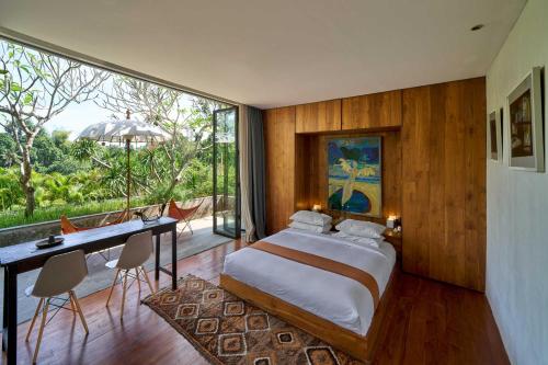 a bedroom with a bed and a desk and a large window at Chameleon Villa Bali in Tabanan