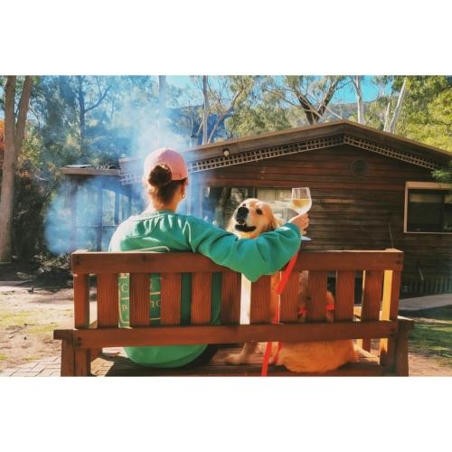 a woman sitting on a bench with a dog holding a glass at Blue Wren Mews in Halls Gap