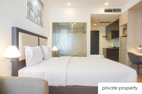 a bedroom with a large white bed and a kitchen at Warm Aston Bellevue HOTEL Apartment - SMART TV in Jakarta