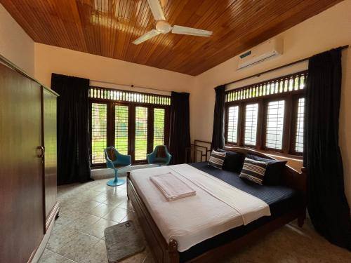 a bedroom with a bed with two chairs and windows at RIVINSON Villa Beruwala in Beruwala