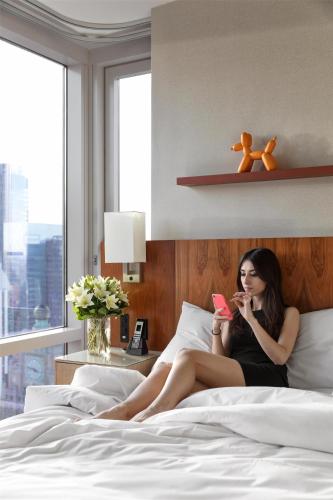 a woman sitting on a bed holding a cell phone at Hyatt Centric Times Square New York in New York