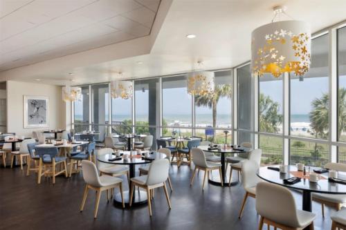 a dining room with tables and chairs and windows at Embassy Suites by Hilton Myrtle Beach Oceanfront Resort in Myrtle Beach