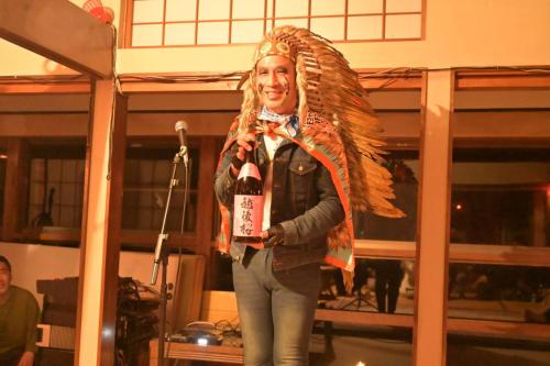 a woman standing on a stage holding a bottle of wine at わくわく自然体験の宿ゲストハウス山楽 in Itoigawa