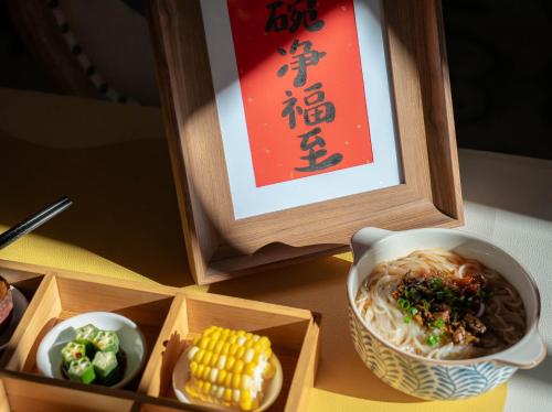a bowl of noodles and corn on a table with a sign at 指云公馆Lijiang Mufu Royal Garden Resort半山观景民宿 in Lijiang