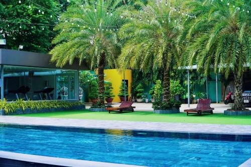a pool with two chairs and palm trees next to a building at The Mira Boutique Hotel in Thu Dau Mot