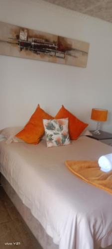 a white bed with orange pillows on top of it at Zuzani Ikhaya B&B in Grahamstown