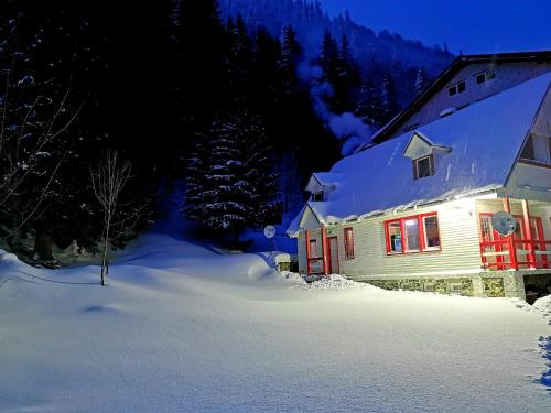a snow covered house with red shutters in the snow at Cabana Dara in Cumpăna