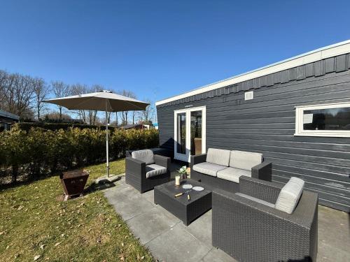 a patio with two couches and an umbrella at Spa Chalet Veluwe Wellness with Private HOTTUB and SAUNA - Family Holiday House with Fenced Garden - Veluwe Holiday Putten in Putten