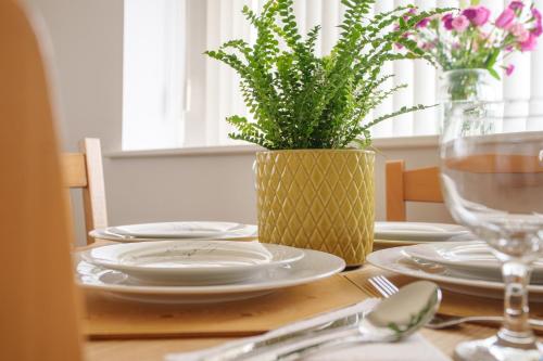 a table with plates and a vase with a plant at 2-bedroom apartment in Headington with free parking, walking distance to Oxford Hospitals & Brookes Uni in Oxford