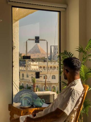 a man sitting at a table looking out a window at a pyramid at Fancy Pyramids View Khan Giza's Gem in Cairo