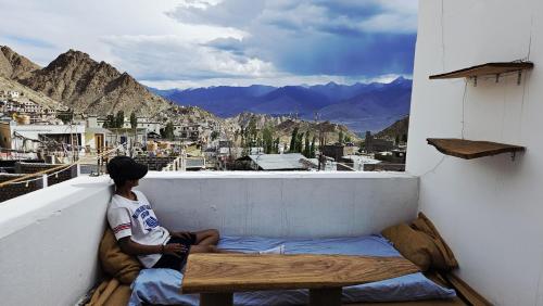 a young boy sitting on a balcony looking out at the mountains at Hearth and Haven Homestay in Leh