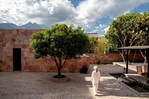 Eine Person geht durch einen Innenhof mit einem Baum in der Unterkunft Mucheng Xichi Snow Mountain Art Resort Hotel (Baisha Ancient Town Branch) in Lijiang