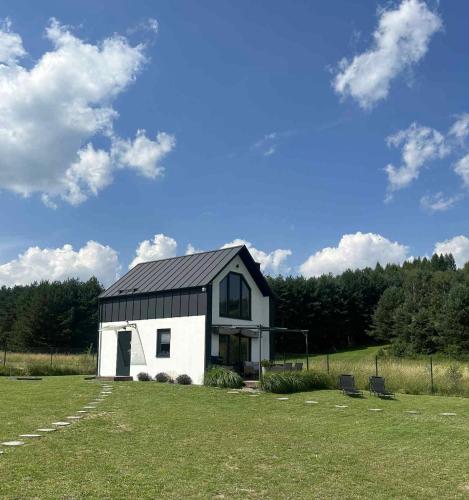 a small white house with a black roof in a field at Perły Roztocza - Domek całoroczny in Krasnobród