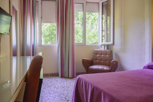 a bedroom with a bed and a chair and windows at Hotel Paraíso in Lanjarón