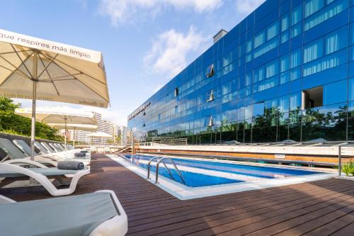 a swimming pool with chairs and an umbrella next to a building at Abba Playa Gijón in Gijón