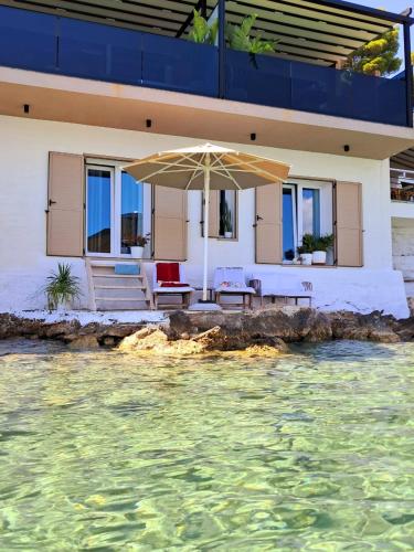 a house with a table and an umbrella over the water at Artis Blue Relax in Himare