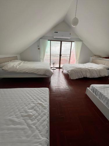 a attic bedroom with three beds and a window at Baan Plumeria บ้านภูมิเรีย in Phetchaburi
