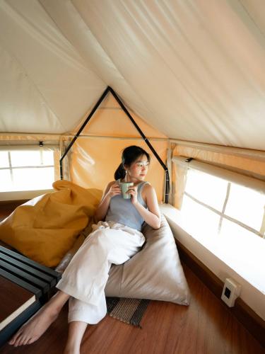 a woman sitting on a bed in a tent holding a cup at Berghaus101khaoyai in Nakhon Ratchasima
