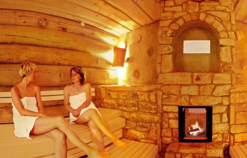 two women sitting in a sauna with a fireplace at Hasseröder Ferienpark in Wernigerode