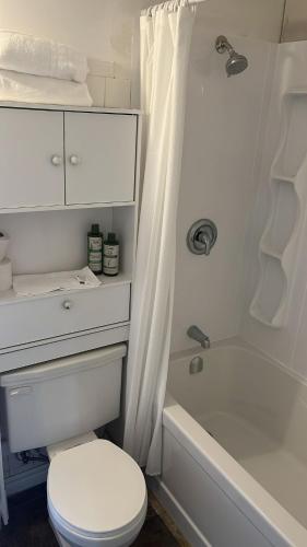 a white bathroom with a toilet and a bath tub at Auberge Notre-Dame in Kedgwick
