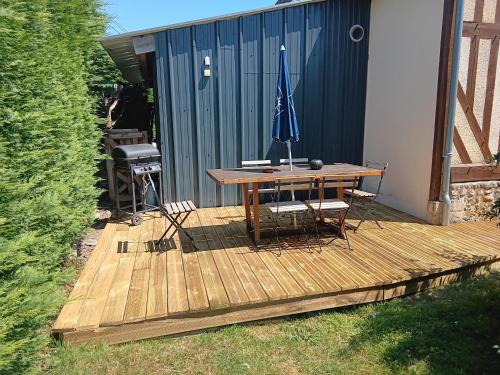 une terrasse en bois avec une table, des chaises et un parasol dans l'établissement Augettes Etable, à Saint-Hymer