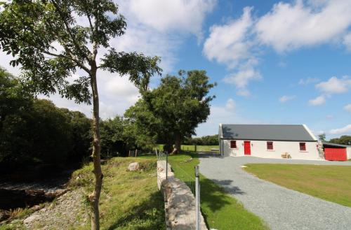 a white barn with a fence next to a road at Kate's Cottage in Louisburgh