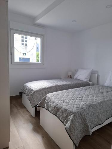 a white bedroom with two beds and a window at Casa Machado in Cangas de Morrazo