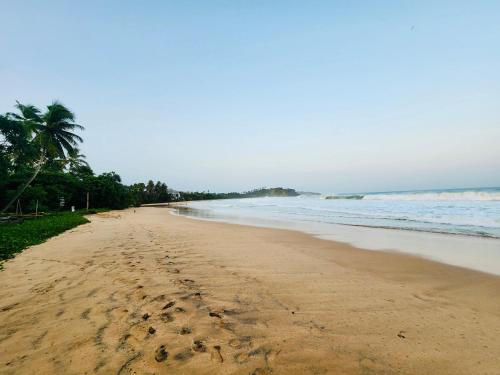 a beach with footprints in the sand and the ocean at Seven Shape Resort - Talalla in Talalla